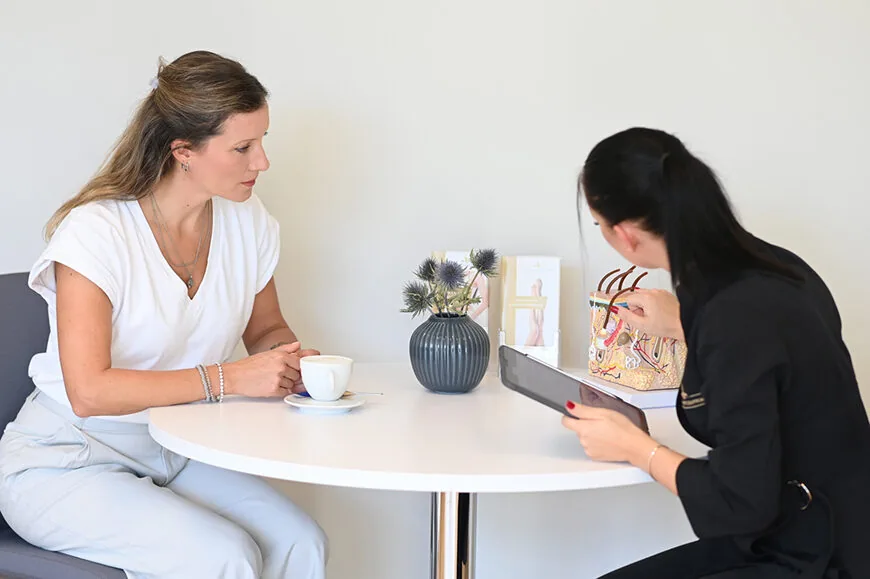 Beratungsgespräch in einer ästhetischen Praxis: Eine Fachkraft erklärt einer Patientin mithilfe eines anatomischen Modells und eines Tablets mögliche Behandlungsoptionen.